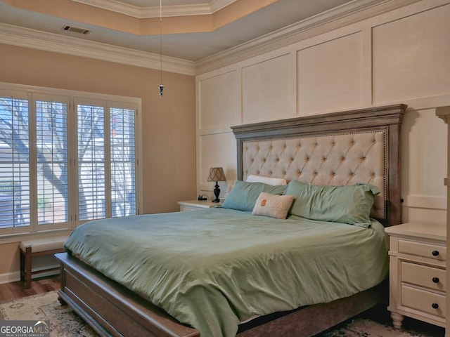 bedroom featuring light wood-style flooring, visible vents, a tray ceiling, and ornamental molding