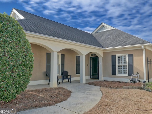 entrance to property featuring roof with shingles and stucco siding