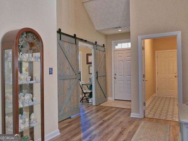 entrance foyer with light wood finished floors, a barn door, visible vents, and a textured ceiling