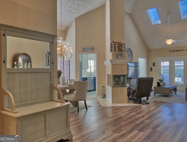 dining space featuring a skylight, a tiled fireplace, high vaulted ceiling, and wood finished floors