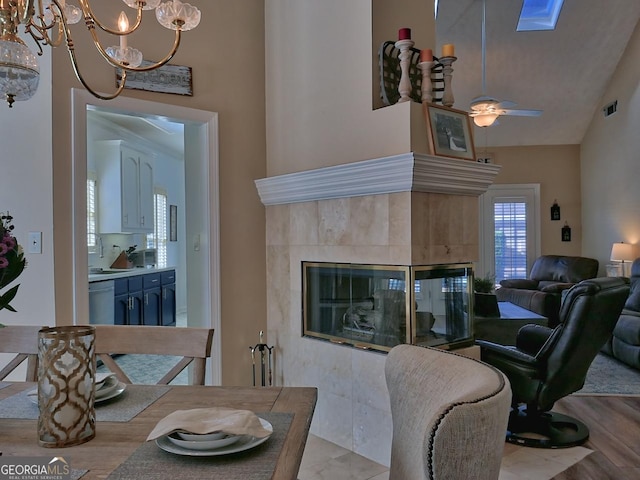 living area featuring ceiling fan with notable chandelier, a towering ceiling, visible vents, light wood-style floors, and a tiled fireplace