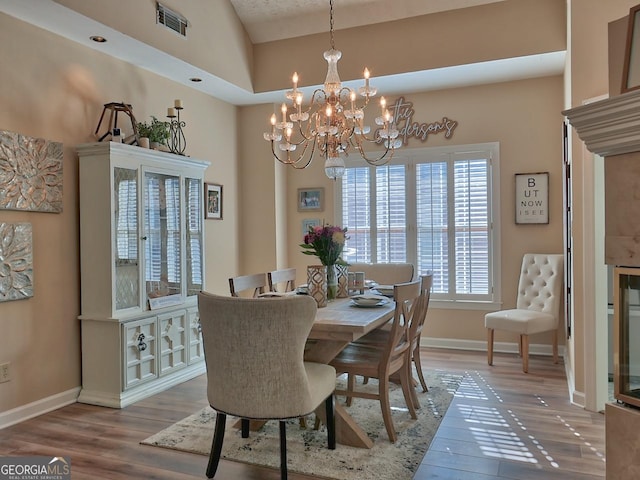 dining space with a notable chandelier, baseboards, visible vents, and wood finished floors