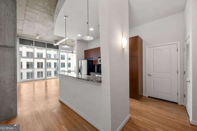 kitchen featuring stone countertops, light wood-type flooring, stainless steel fridge, and decorative light fixtures