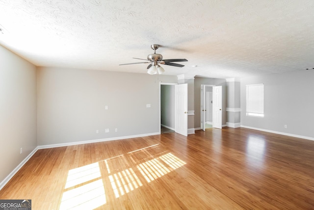 interior space with ceiling fan, a textured ceiling, baseboards, and wood finished floors