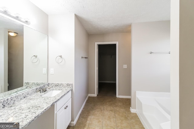 bathroom featuring a textured ceiling, vanity, a bath, baseboards, and tile patterned floors