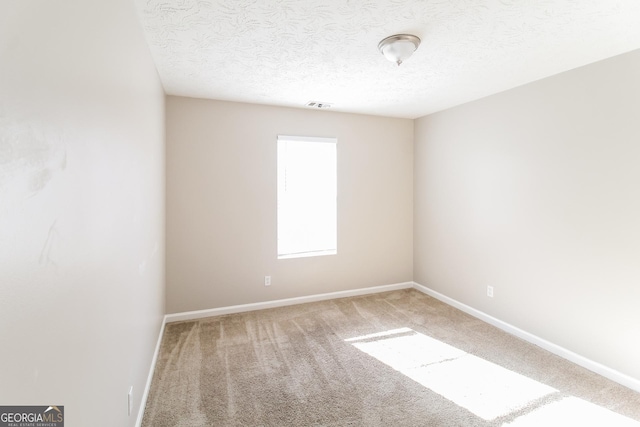 empty room featuring a textured ceiling, carpet, visible vents, and baseboards