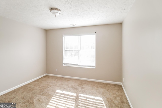 empty room featuring light colored carpet, visible vents, a textured ceiling, and baseboards