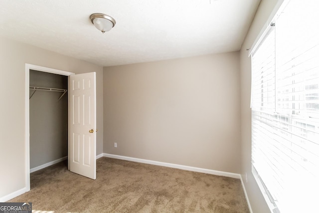 unfurnished bedroom with a closet, light colored carpet, and baseboards