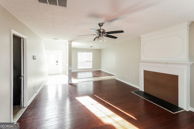 unfurnished living room featuring ceiling fan, a textured ceiling, visible vents, dark wood finished floors, and decorative columns