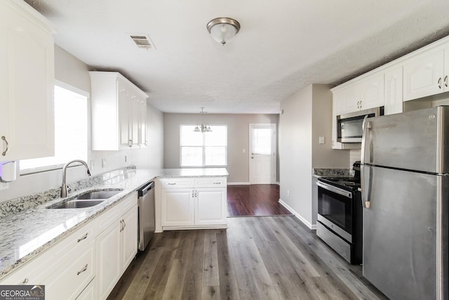 kitchen with a peninsula, appliances with stainless steel finishes, a sink, and white cabinets