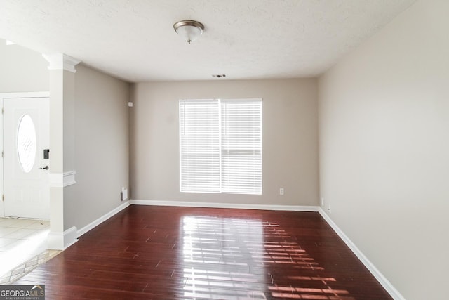 empty room with decorative columns, a textured ceiling, baseboards, and wood finished floors