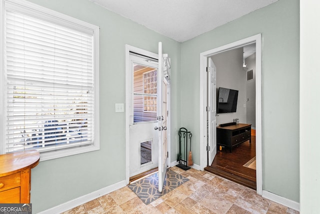 entryway featuring a textured ceiling, stone finish flooring, visible vents, and baseboards