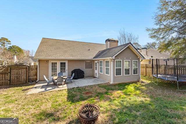 back of property with a trampoline, a patio, a chimney, a gate, and a fenced backyard