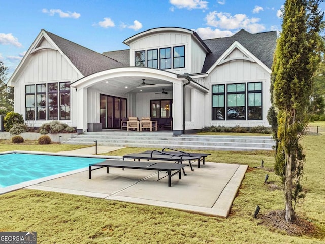 rear view of house with a ceiling fan, a yard, an outdoor pool, and board and batten siding