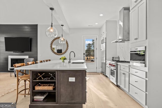 kitchen featuring light countertops, hanging light fixtures, a sink, wall chimney range hood, and high quality appliances