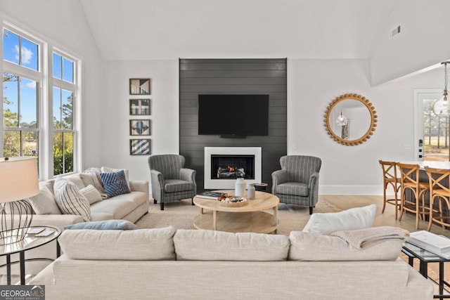 living room featuring a large fireplace, baseboards, visible vents, light wood-style floors, and high vaulted ceiling