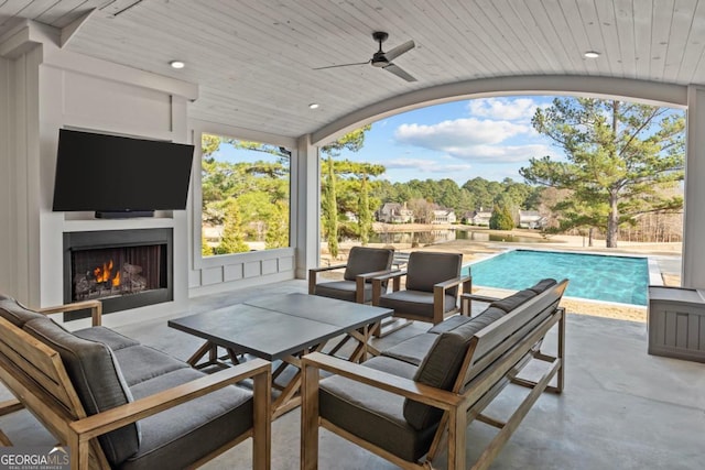 view of patio / terrace with a warm lit fireplace, ceiling fan, and an outdoor pool