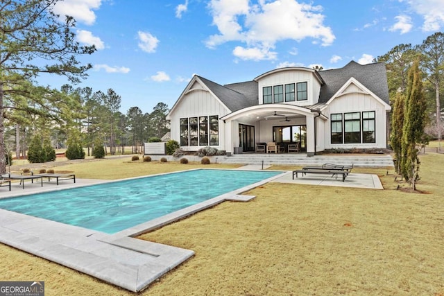 back of house with a patio, a lawn, a ceiling fan, board and batten siding, and an outdoor pool