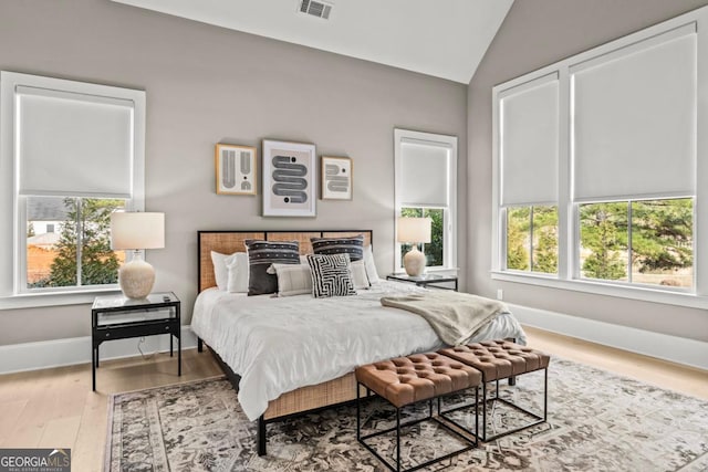 bedroom featuring multiple windows, vaulted ceiling, visible vents, and wood finished floors