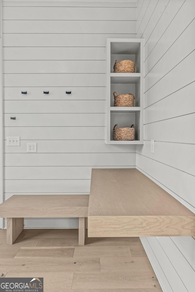 mudroom with built in features, wooden walls, and wood finished floors