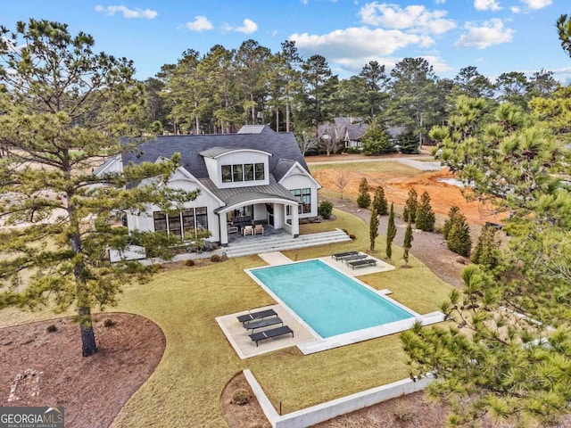 rear view of house featuring an outdoor pool, metal roof, a standing seam roof, a yard, and a patio area