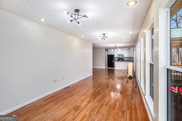 unfurnished living room featuring a textured ceiling, wine cooler, light wood-style flooring, recessed lighting, and baseboards