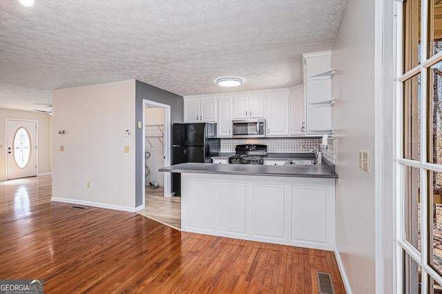 kitchen with dark countertops, stainless steel microwave, stove, a peninsula, and white cabinetry