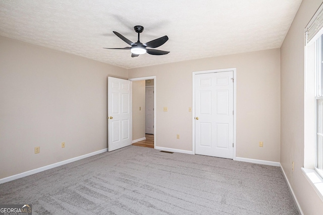 unfurnished bedroom with a textured ceiling, ceiling fan, light colored carpet, visible vents, and baseboards