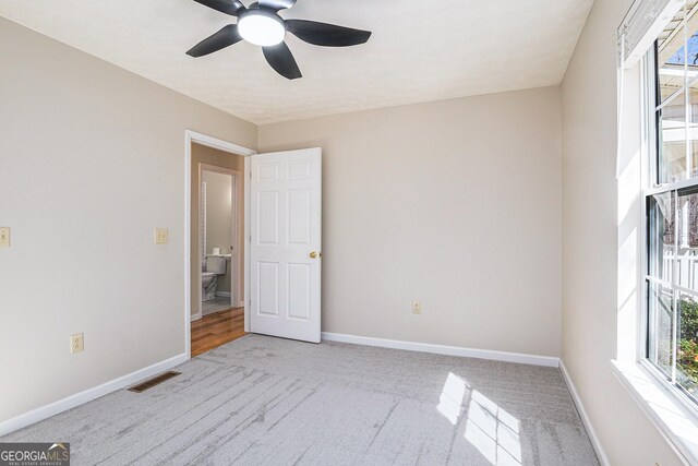 spare room with light colored carpet, ceiling fan, visible vents, and baseboards