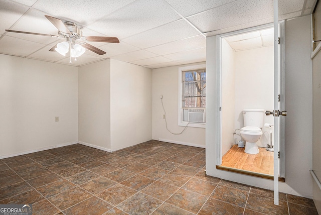 unfurnished room with ceiling fan, stone finish flooring, a drop ceiling, and baseboards