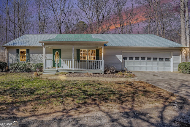 ranch-style home with a porch, concrete driveway, a lawn, an attached garage, and metal roof