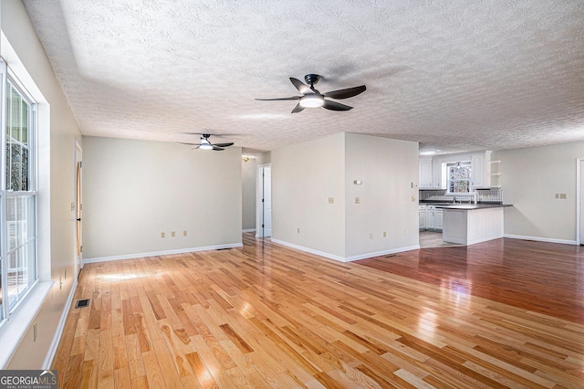 unfurnished living room featuring light wood-style floors, visible vents, ceiling fan, and baseboards