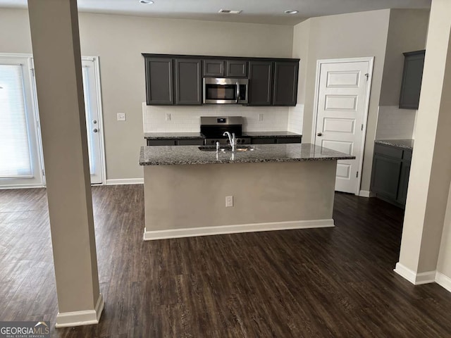 kitchen with visible vents, dark stone counters, dark wood-type flooring, a kitchen island with sink, and stainless steel appliances