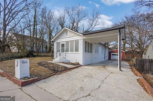 bungalow-style home featuring aphalt driveway, an outdoor structure, fence, and brick siding