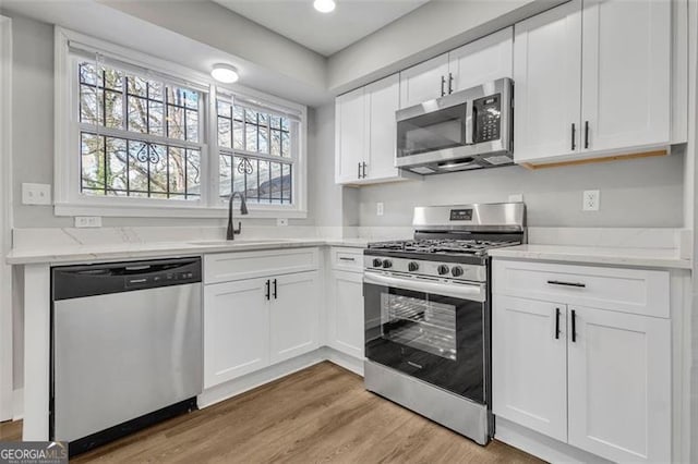 kitchen with white cabinets, light stone countertops, stainless steel appliances, light wood-type flooring, and a sink