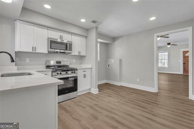 kitchen with stainless steel appliances, white cabinets, a sink, and light stone counters