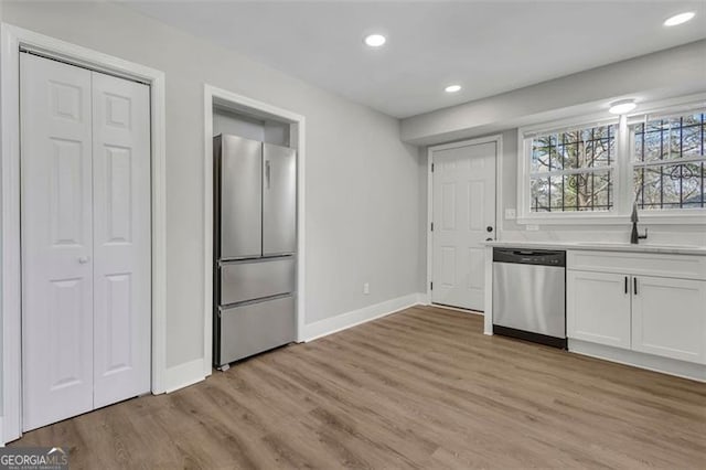 kitchen with light wood-style flooring, appliances with stainless steel finishes, light countertops, white cabinetry, and a sink