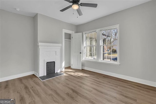 unfurnished living room featuring a brick fireplace, ceiling fan, baseboards, and wood finished floors