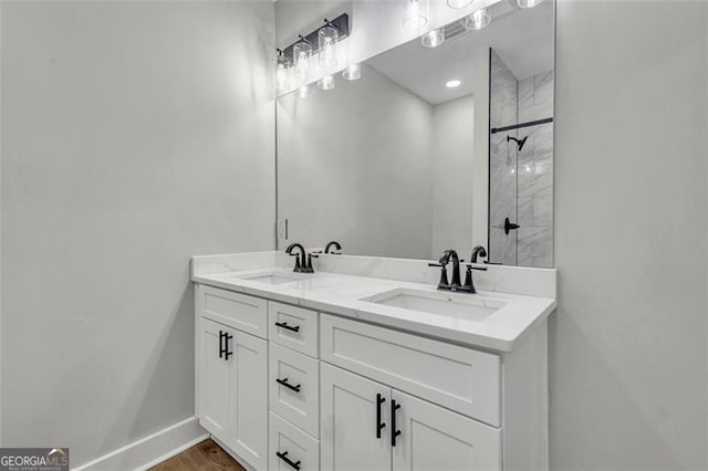 full bath featuring a sink, a tile shower, baseboards, and double vanity