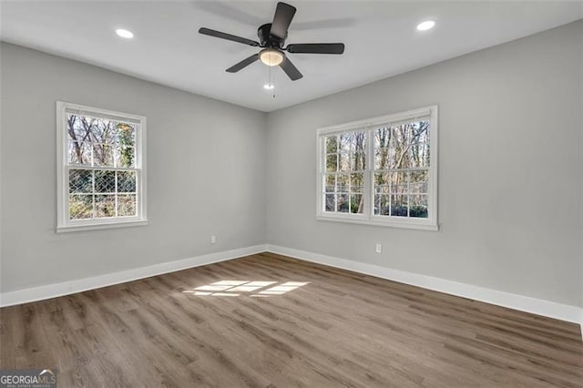 empty room with recessed lighting, wood finished floors, a wealth of natural light, and baseboards