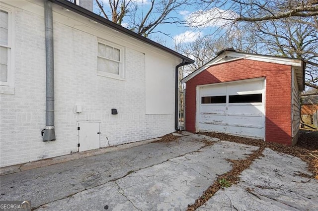 view of side of property with concrete driveway, brick siding, a detached garage, and an outdoor structure