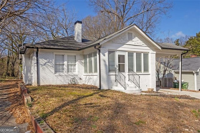 view of front of house featuring entry steps, a front yard, a chimney, and brick siding