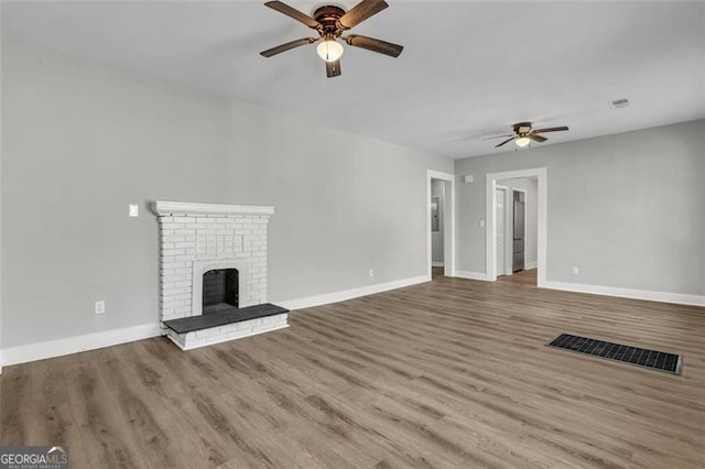 unfurnished living room featuring a fireplace, visible vents, ceiling fan, wood finished floors, and baseboards