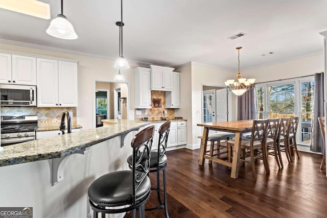 kitchen featuring stainless steel appliances, white cabinetry, decorative light fixtures, and light stone counters