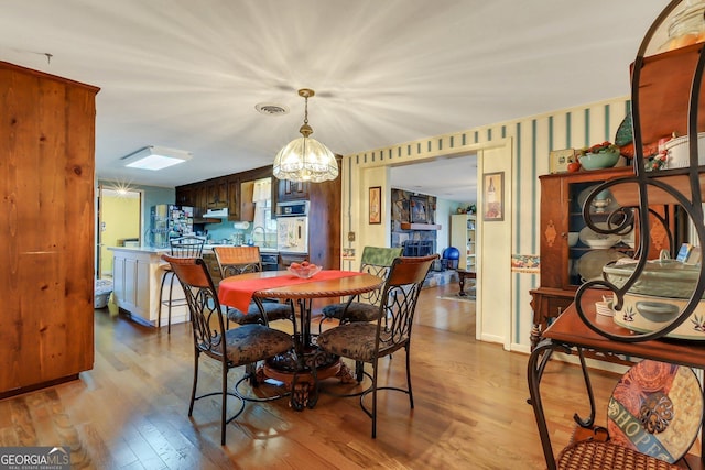 dining space featuring a stone fireplace, light wood-type flooring, visible vents, and an inviting chandelier