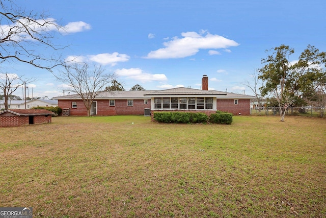 rear view of house featuring a sunroom, a chimney, fence, a yard, and brick siding