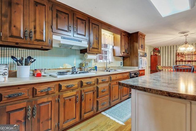 kitchen with decorative light fixtures, dark countertops, white gas cooktop, a sink, and under cabinet range hood