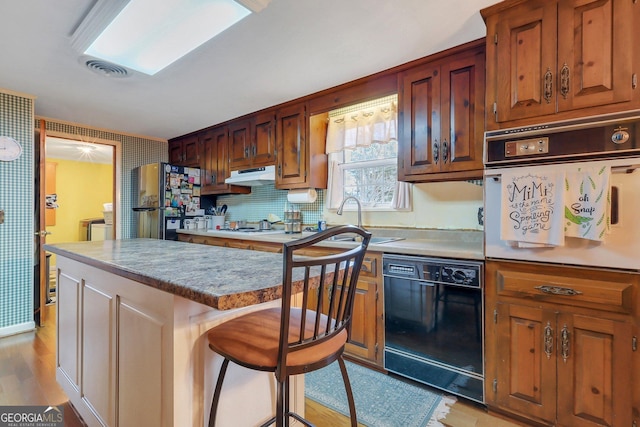 kitchen with white appliances, a breakfast bar, light countertops, under cabinet range hood, and a sink