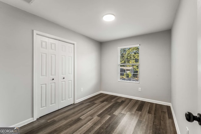 unfurnished bedroom with dark wood-style floors, baseboards, and a closet