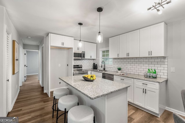 kitchen with white cabinets, dark wood-style flooring, a sink, stainless steel appliances, and backsplash